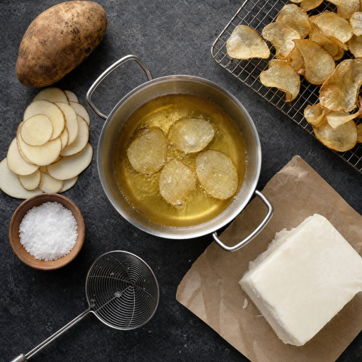 Potatoes being sliced and fried in beef tallow, with a block of tallow, salt and finished chips